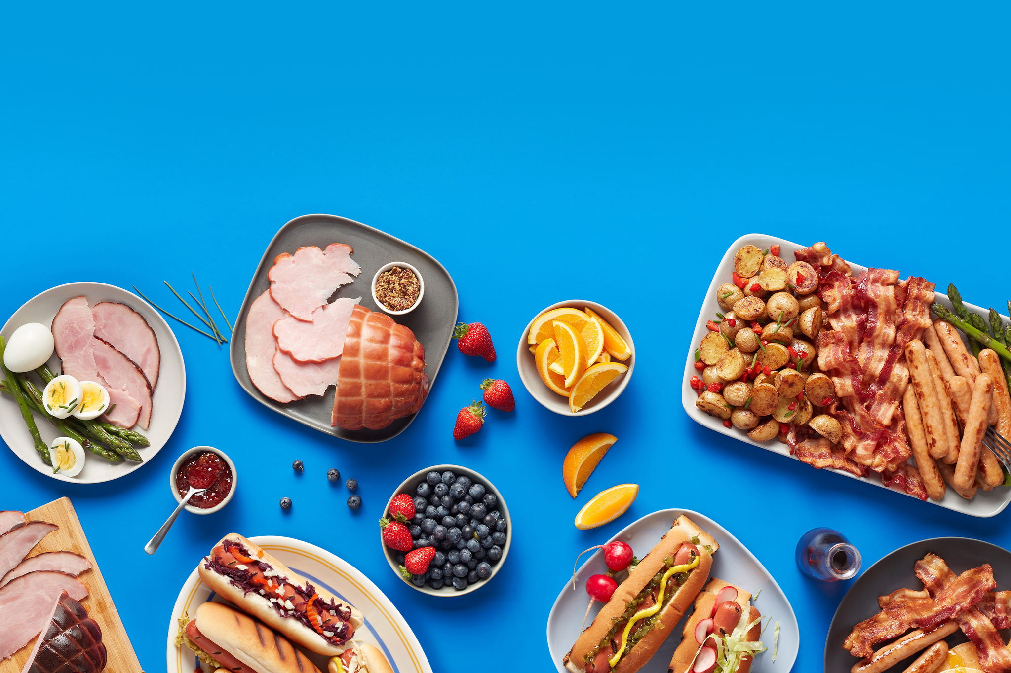 Tablée avec différents plats de saucisses, bacons, jambons, hotdog, patates et fruits