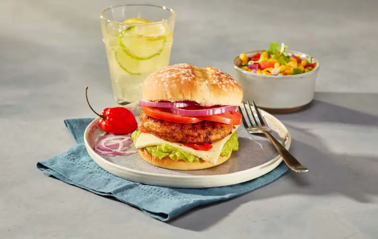 Burger de poulet assaisonné garni d'oignons rouges, tomates, fromage, piment fort et laitue
