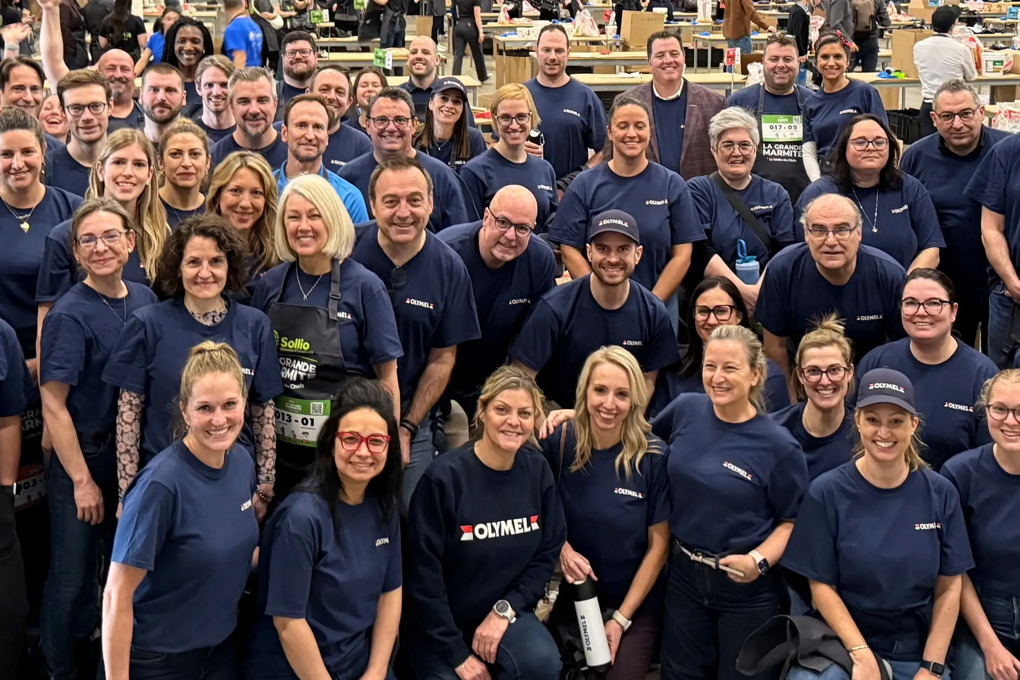 Un grand groupe de personnes portant des chemises bleues assorties pose ensemble dans un vaste espace intérieur, souriant à la caméra.