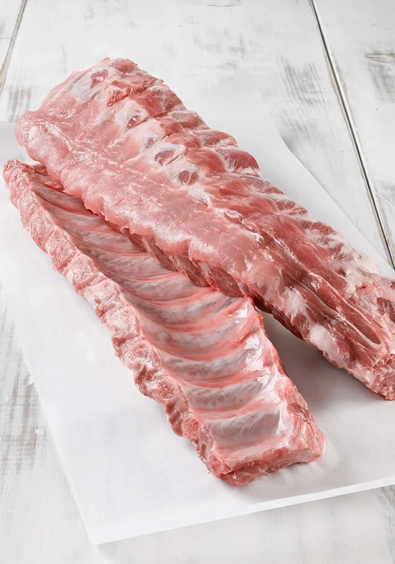 Deux carrés de côtes de porc crus sur papier blanc.