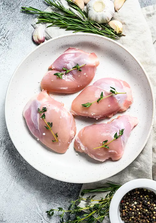 Quatre hauts de cuisse de porc sur une assiette, entourée d’herbes, d’ail et de poivre.