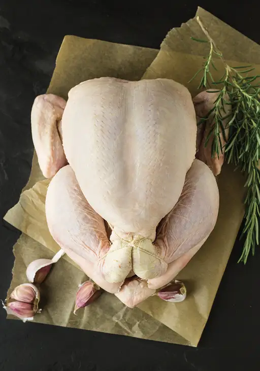Poulet entier cru sur papier parchemin, avec ail et romarin.