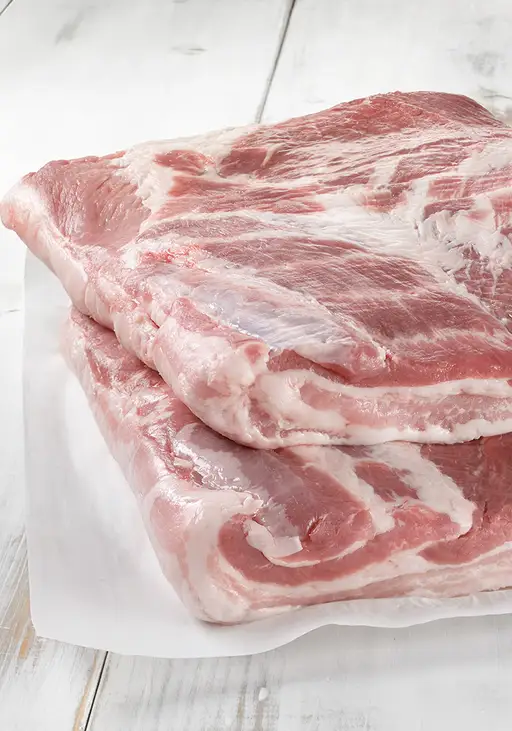 Deux demi-flancs de porc crus sur papier blanc.