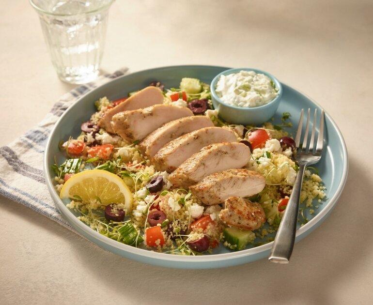 Tranches de poitrine de poulet grillée sur couscous avec légumes, citron et sauce tzatziki.
