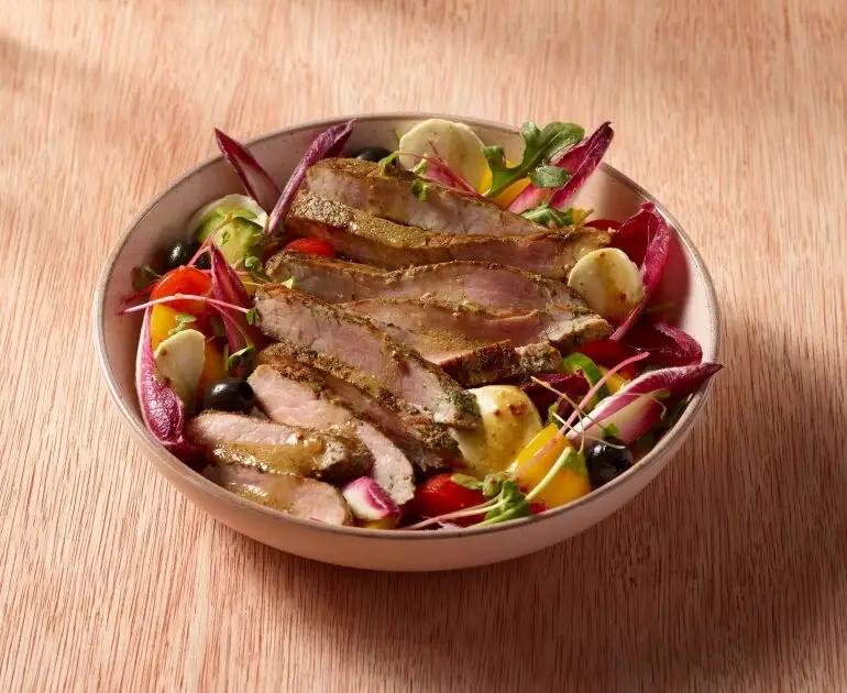 Bol de viande cuite en tranches avec légumes variés, tomates cerises, radis, olives et légumes verts.