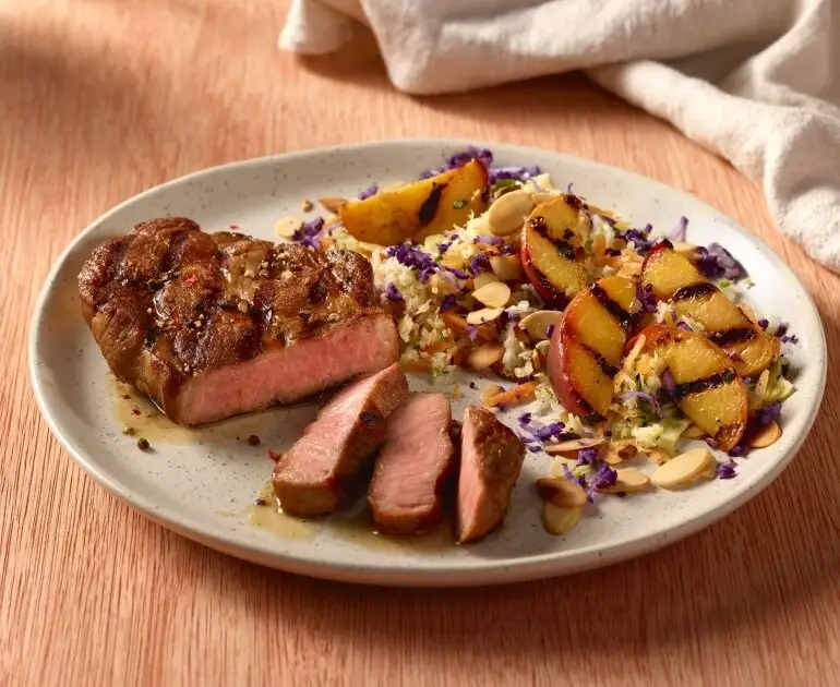 Tranches de porc grillées avec salade de choux, pêches et amandes.