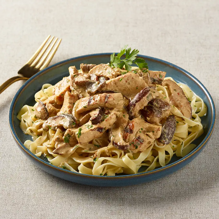 Lanières de poitrine de poulet à la crème de champignons et moutarde servies sur des pâtes longues dans une assiette bleue avec une fourchette or