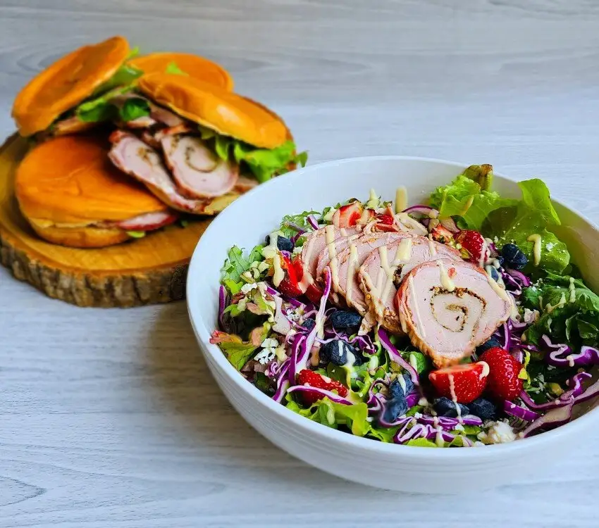 Bol de salade avec fraises, myrtilles et porc, et deux sandwiches.