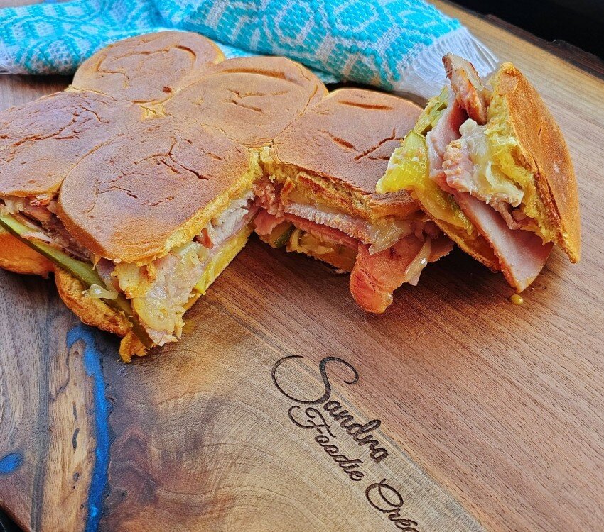 Sandwich coupé en quartiers sur une planche à découper en bois, avec viande, fromage et cornichons.
