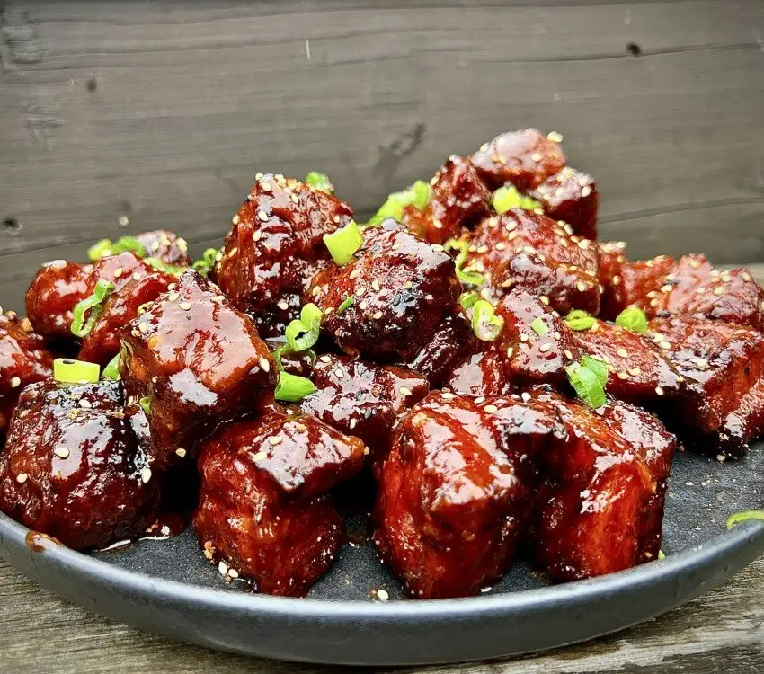 Cubes de viande glacés garnis d'oignons verts hachés et de graines de sésame.