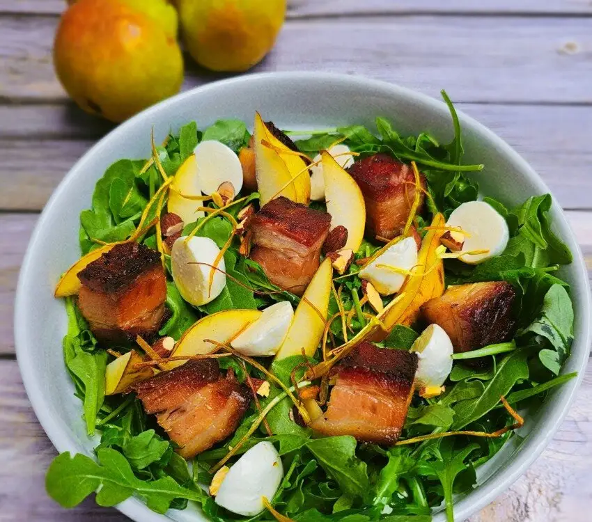 Bol de salade avec porc grillée, poires, fromage et noix.