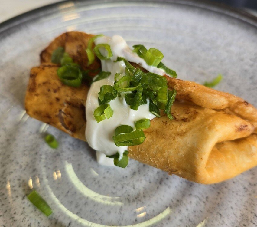 Chimichanga frit roulé avec crème sure et oignons verts hachés.