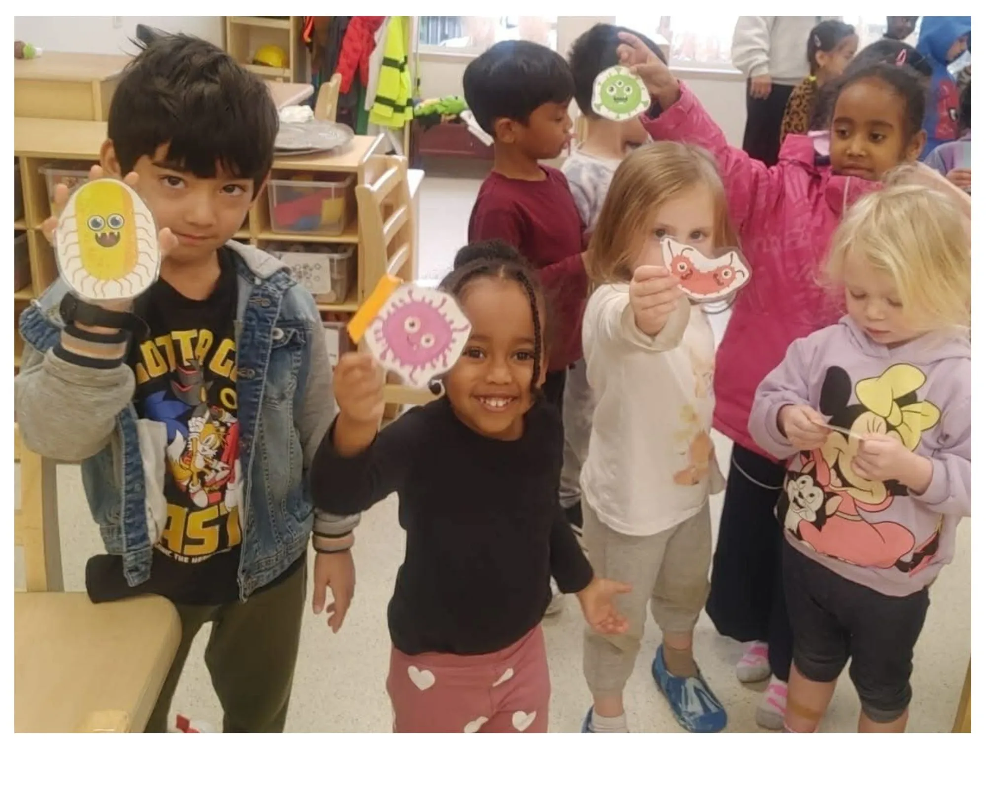 A group of children hold paper cut-outs of animated “germs” as part of a hand hygiene education campaign.