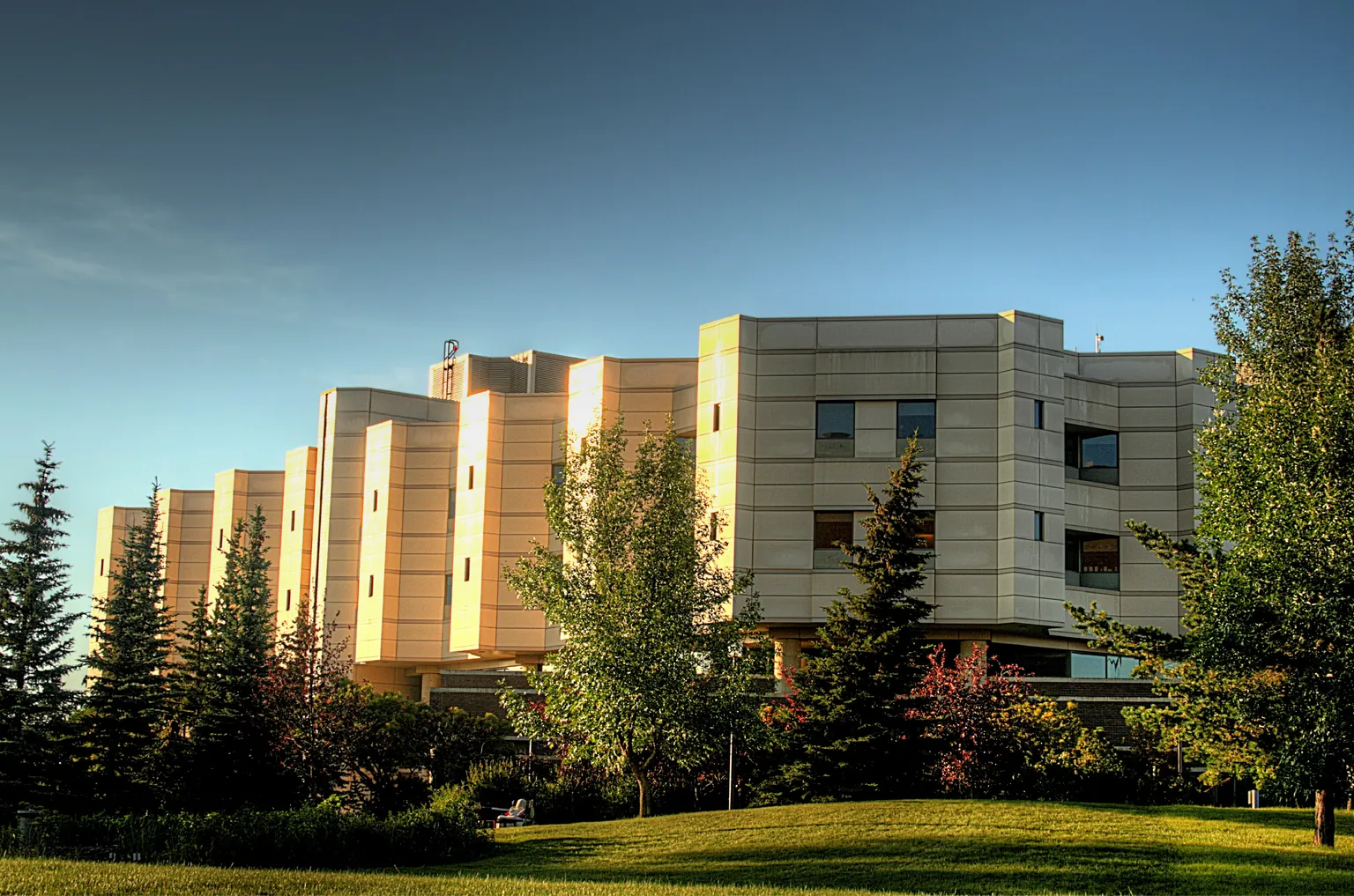 A photo of Edmonton’s Glenrose Rehabilitation Hospital. The hospital is in the background with the sun lighting up the west side of the building. There is vegetation around the hospital.